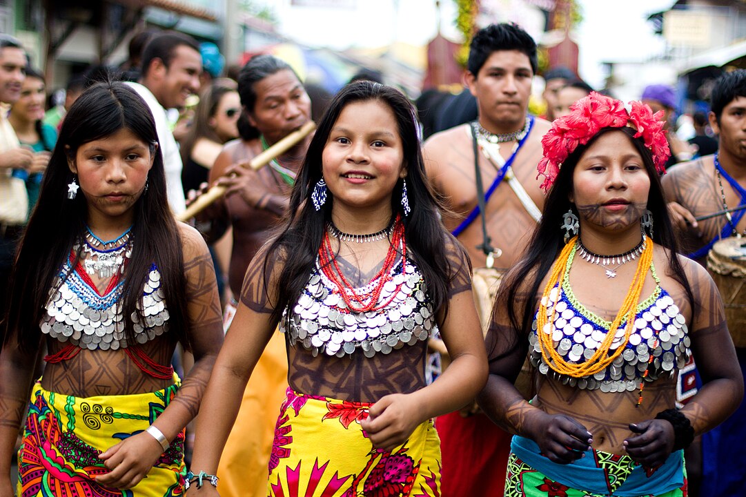 Three young women in traditional colorful attire standing in a crowd.