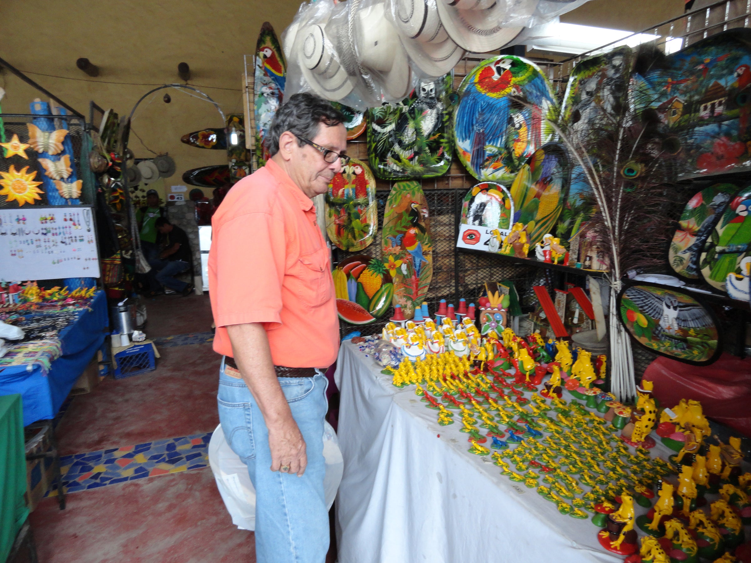 Man in an orange shirt standing in front of a colorful display of souvenirs and decorations.