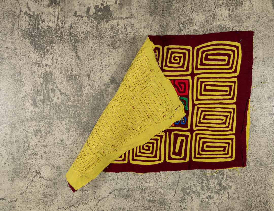Hand stitched Guna mola from Guna Yala Panama, yellow spiral border running around the maroon center